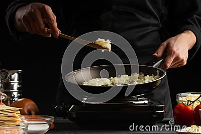 Chef fries onions in a pan, against the background of ingredients. Home recipe book, delicious food, gastronomy Stock Photo
