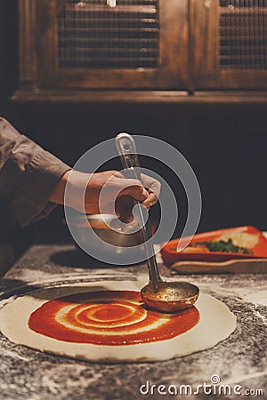 Chef hand spreading tomato paste on pizza base Stock Photo