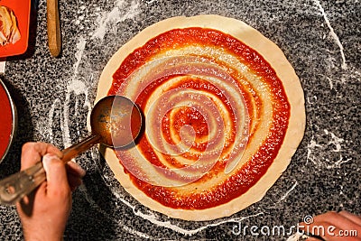 Chef hand spreading tomato paste on pizza base Stock Photo