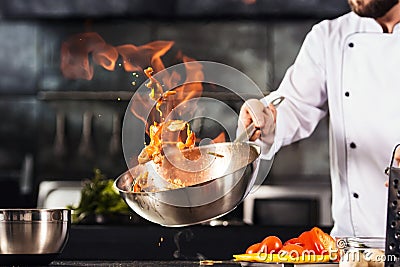 Chef hands keep wok with fire. Closeup chef hands cook food with fire. Stock Photo