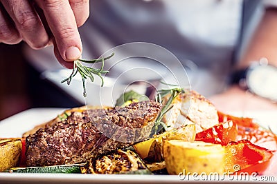 Chef in hotel or restaurant kitchen cooking only hands. Prepared beef steak with vegetable decoration Stock Photo