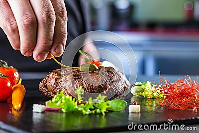 Chef in hotel or restaurant kitchen cooking, only hands. Prepared beef steak with vegetable decoration Stock Photo