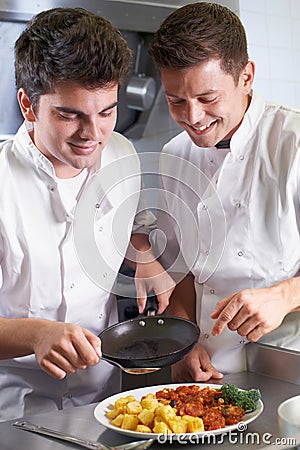 Chef Instructing Male Trainee In Restaurant Kitchen Stock Photo