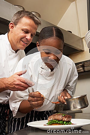 Chef Instructing Trainee In Restaurant Kitchen Stock Photo