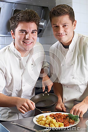 Portrait Of Chef Instructing Trainee In Restaurant Kitchen Stock Photo