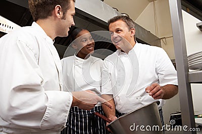 Chef Instructing Trainees In Restaurant Kitchen Stock Photo