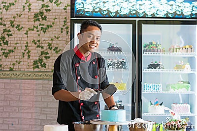 Asian male pastry chef wearing black uniform pouring melted chocolated to round blue cake Stock Photo