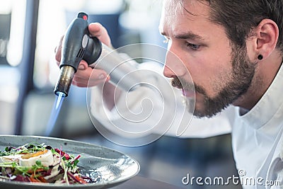 Chef preparing food. Cook flamed using FlambÃ© gun pistol. Chef flambe vegetable salad with goat cheese. Gourmet cuisine Stock Photo