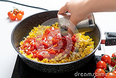 The Chef Puts the Tomatoes in their own juice into a Pan with Chopped Bell Peppers and Onions, which are fried on the Stove. Stock Photo
