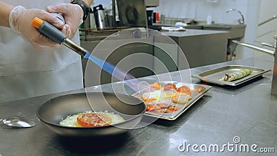 The chef roasts the ingredients to decorate the dish. Strawberries are baked with fire, close-up. Restaurant kitchen Stock Photo