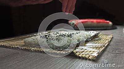Chef`s hands sprinkle sesame seeds on the inside out sushi. Japanese chef in black gloves at work preparing sushi roll Stock Photo