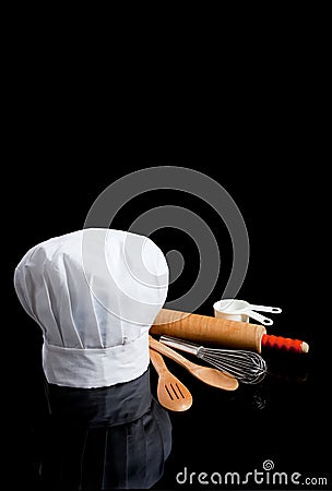 A chef's toque with kitchen utensils on black Stock Photo