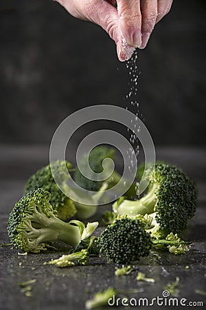 Chef is salting grilled broccoli pieces on the kitchen table. Stock Photo