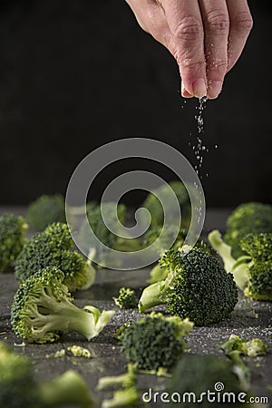 Chef is salting grilled broccoli pieces on the kitchen table. Stock Photo