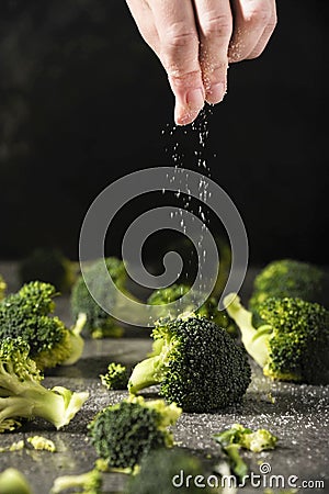 Chef is salting grilled broccoli pieces on the kitchen table. Stock Photo