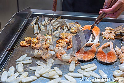 Chef using spatula frying seafood in buffet restaurant`s kitchen Stock Photo