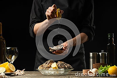 Chef watering raw oyster with lemon juice, with dry Italian wine, for cooking and cooking on a black background, Concept menu, Stock Photo