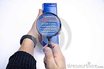 Chemical components on the shampoo label: Sodium Lauryl Sulfate sls, sles. A hand holds a blue jar and a magnifier, where the Stock Photo