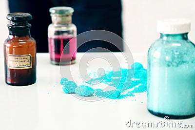 Chemistry bottles containing various substances of different colors standing on laboratory table seen along a pile of blue powder Stock Photo