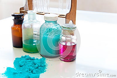 Chemistry bottles containing various substances of different colors standing on laboratory table seen over a pile of blue powder Stock Photo