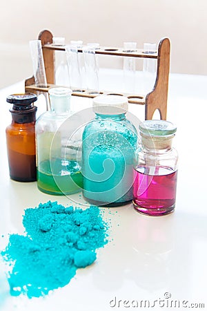 Chemistry bottles containing various substances of different colors standing on laboratory table seen over a pile of blue powder Stock Photo