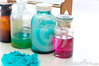 Chemistry bottles containing various substances of different colors standing on laboratory table seen over a pile of blue powder Stock Photo