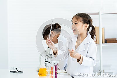 In chemistry classroom with many laboratory tools. Two little Asian girls in white lab coat help each other do experiment. A girl Stock Photo