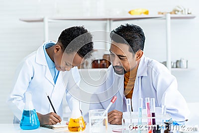 .In chemistry classroom with many laboratory tools. A young African boy and male teacher in white lab coat help Stock Photo