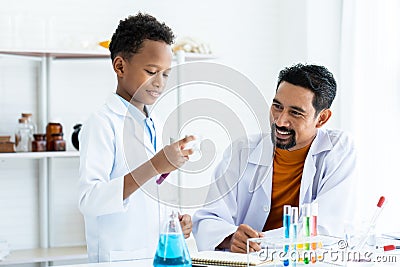 In chemistry classroom with many laboratory tools. A young African boy with teacher in white lab coat do experiment together. A Stock Photo