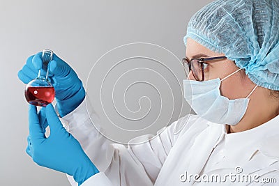 In a chemistry lab, a female pharmacist is analyzing a flask with red liquid. Medical experiment with a tube. Stock Photo