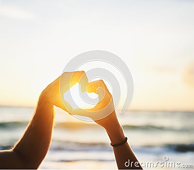 Cherish every sunset. a couple forming a heart shape with their hands at the beach. Stock Photo