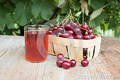 Cherry berry. Harvest cherries in a basket on a wooden background. A glass of fresh cherry juice, fruit drink. Stock Photo