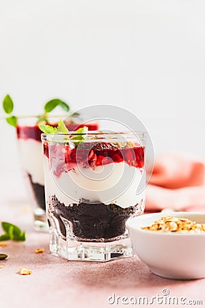 Cherry, cream cheese and chocolate biscuit portion layered dessert in glass, pink background. Black forest trifle. Summer dessert Stock Photo