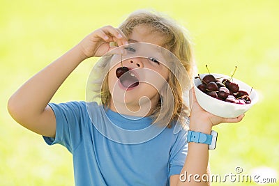 Cherry and cute child. Happy little child with cherry outdoors. Kid picking and eating ripe cherries in summer park Stock Photo