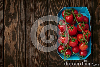 Cherry tomato branches in cardboard packing tray on wooden background Stock Photo