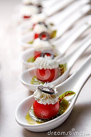 Cherry tomatoes on dessert spoons, garnished with buttercream and sliced olives Stock Photo