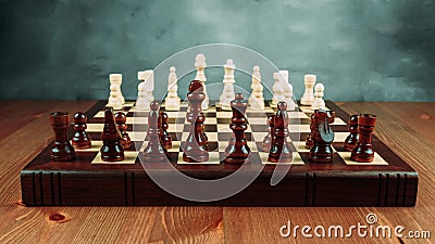 A chessboard made of wood with chess pieces placed on it stands on a table Stock Photo