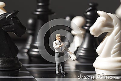 Chessman and chess figures on game board. Playing chess with miniature doll macro photo. Stock Photo