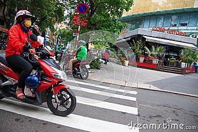 Ho Chi Minh city, Vietnam - December 2018: woman on motorbike crossing crosswalk near Saigon Skydeck. Editorial Stock Photo