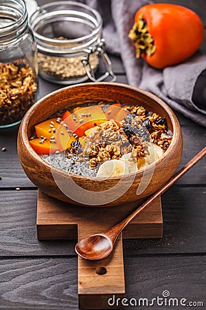 Chia pudding with banana, persimmon and granola, dark wooden background. Stock Photo