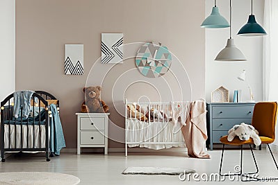 Chic baby bedroom with wooden cribs, lamps, white wooden nightstand with brown teddy bear and fashionable yellow chair Stock Photo