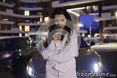 Chic girl drinks a drink in a glass on the street near the car, a golden car, Dubai. Stock Photo