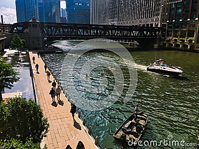 Chicago River during a colorful summer, people on riverwalk, man fishes out of parked fishing boat, kayakers and speedboat pass Editorial Stock Photo