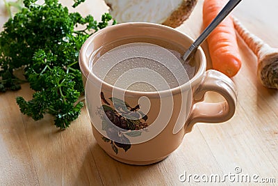 Chicken bone broth in a mug with vegetables in the background Stock Photo