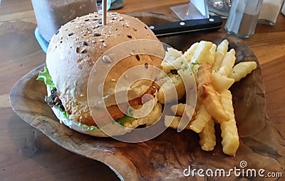 Chicken burger and fries hot potato chips with lettuce on a wooden plate. Stock Photo