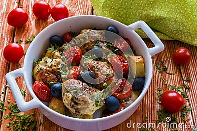 Chicken legs with potatoes, cherry tomatoes and black olives. White baking dish on wooden background Stock Photo