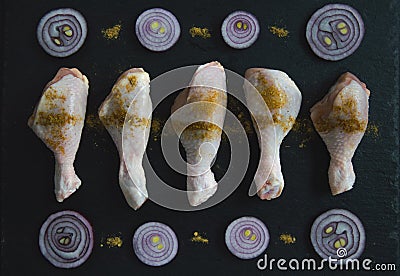 Chicken legs with spices and red onions lie on a black stone board. Cook chicken legs Stock Photo
