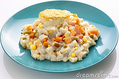 Chicken with mixed vegetables and a biscuit on a blue plate sitting on a white kitchen table waiting to be eaten Stock Photo