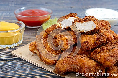 Chicken nuggets. Pieces of deep-fried crispy meat, on paper with different sauces on a wooden table. Stock Photo