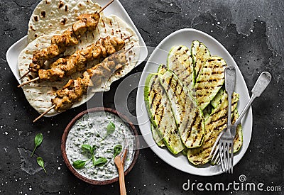 Chicken skewers, grilled zucchini, tortillas and tzadziki sauce - delicious greek style lunch on a dark background, top view Stock Photo